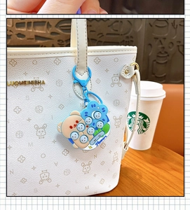 Close-up of a cute bear whack-a-mole game keychain hanging on a stylish white handbag.