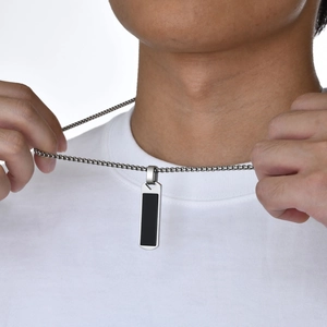 Close-up of a men's rectangular black pendant necklace with silver chain on a model
