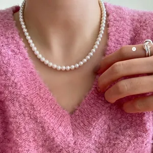 Close-up of elegant white pearl necklace and silver knot ring worn with pink knit sweater