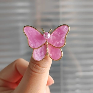 Detailed close-up of pink shell butterfly brooch with gold plating and center pearl accent