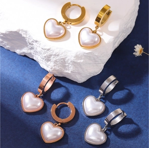 Close-up of heart-shaped pearl earrings in gold, silver, and rose gold on a stone base