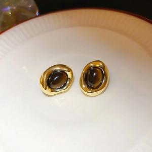 Close-up of vintage oval gold-plated stud earrings with brown stone on a ceramic plate