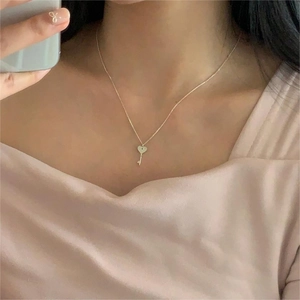 Close-up of minimalist heart-shaped key pendant necklace in gold on a female neck