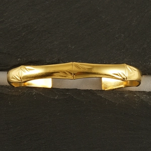 Détail d'un bracelet jonc bambou doré posé sur des pierres grises foncées