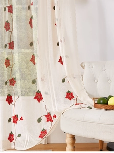 Close-up of lace curtain featuring red floral embroidery and delicate scalloped edges