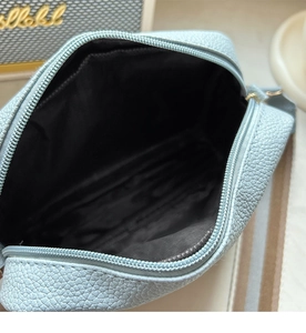 Close-up of light blue litchi grain shoulder bag with zipper and black fabric lining