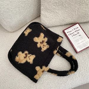 Close-up of black teddy fleece tote bag with bear pattern on soft cream sofa background