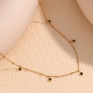Detailed macro view of 18K gold plated necklace with round green zircon stones on beige stone