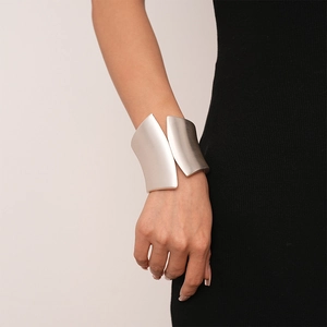 Close-up of a silver matte wide irregular cuff bracelet worn on a model with black dress