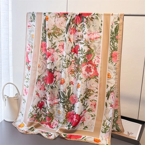 Floral print satin scarf with pink peonies and beige border draped on a display rack