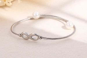 Detail van zilveren infinity armband met gedraaide staalkabel en witte parels aan uiteinden