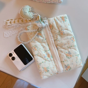 Close-up of quilted floral bag with pearl handle and heart pendant on white background