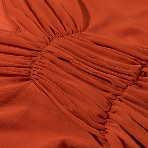 Close-up of pleated texture on orange dress with detailed ruched chiffon fabric pattern