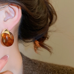 Macro view of C-shaped resin stud earring in amber brown with gold metal detailing
