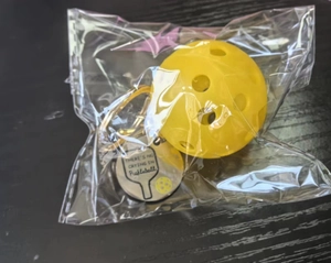 Detail of yellow pickleball keychain with 'THERE'S NO CRYING IN Pickleball' metal tag