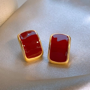 Close-up of elegant red enamel gold rectangular earrings on luxury silver satin fabric