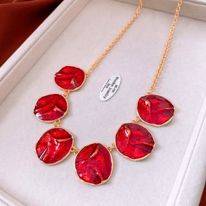 Close-up of vintage gold necklace with red enamel pendants on beige velvet tray