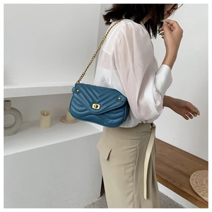 Detail of teal quilted crossbody bag with gold chain strap and metallic twist lock