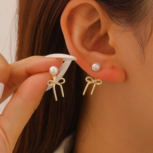 Detailed close-up of elegant pearl bow earrings featuring gold-tone metal drop pendants