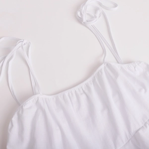Detail of white cotton linen dress showing thin straps and pleated neckline texture