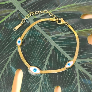 Flat gold snake chain bracelet with evil eye charms on green leaf background