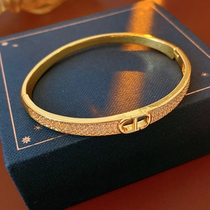 Close-up of gold plated fan-shaped bracelet with D-letter logo and white rhinestones