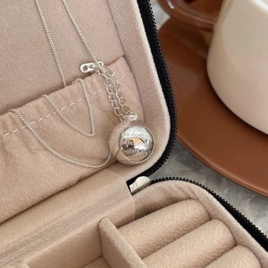 Detail of silver ball pendant necklace engraved with quote in beige jewelry box