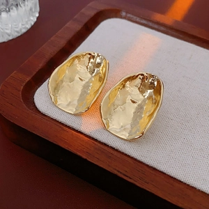 Close-up of golden irregular textured earrings on a premium fabric display tray