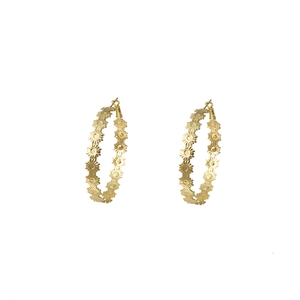 Close-up of golden C-shaped hoop earrings with intricate floral cut-out pattern details