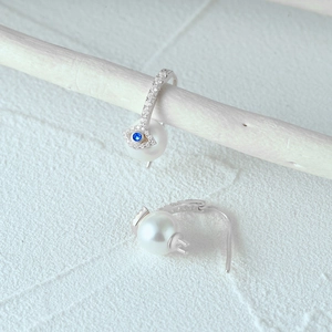 Close-up of 925 sterling silver evil eye earrings with white pearls and blue stones