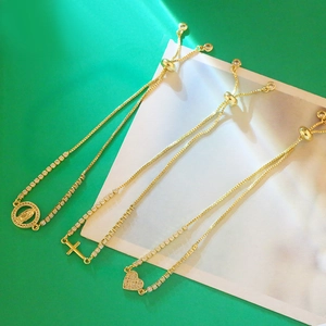 Détail de bracelets dorés ajustables avec breloques cœur en zircon, croix et Marie