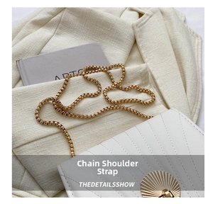 Close-up of a white leather handbag featuring a golden chain strap and shell clasp