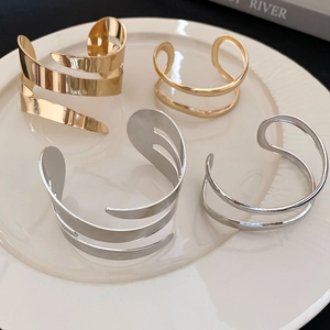Macro detail of gold and silver minimalist layered geometric open bangles on ceramic tray