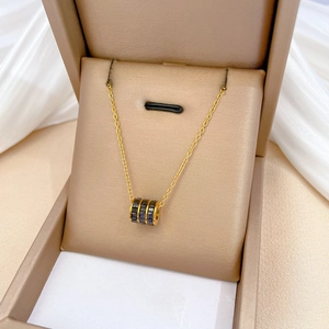 Minimalist gold titanium steel necklace with a black cylinder pendant on soft fabric