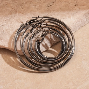 Close-up of three nested gunmetal hoop earrings on a light beige textured stone surface