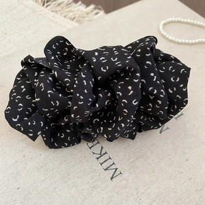 Détail d'un chouchou en tissu noir avec motifs blancs sur une toile beige
