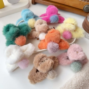 Colorful plush claw hair clips with pom poms in various macaron shades on a tray