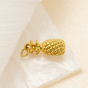 Detailed view of a gold pineapple pendant with fine textures on a soft fabric background