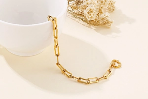 Golden paperclip chain bracelet with OT heart clasp draped over white ceramic cup