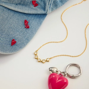 Flat lay of gold heart necklace with zircon stones next to a denim cap and key ring