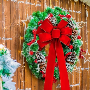 Weihnachtskranz mit roter Samtschleife, Tannenzapfen und Beeren auf Holzgrund