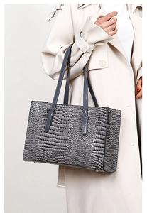 Detail of dark grey crocodile embossed tote bag worn by model in elegant beige coat