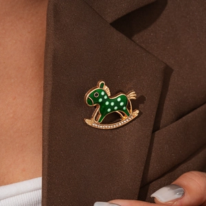 Detail of green enamel rocking horse brooch with crystal inlay on a brown blazer lapel