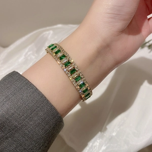 Detailed macro of gold plated bangle with emerald cut green stones and zircon inlay