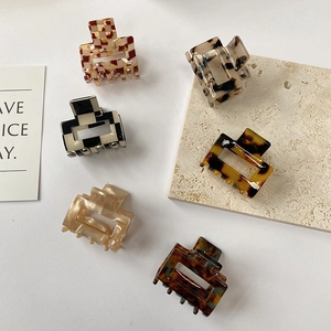 Close-up of six small acetate hair claws in checkered and marble patterns on stone props