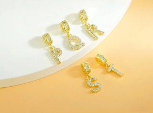 Macro detail of gold-plated P Q R S T letter charms with micro-paved white zircon stones