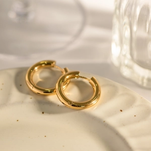 Fashionable gold double-layer stainless steel hoop earrings on a ceramic dish