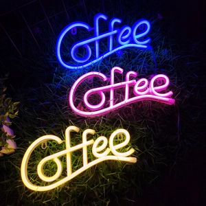 Three LED coffee neon signs in blue, pink, and warm white on grass in a dark outdoor setting