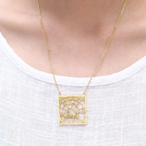 Close-up of golden city map necklace with square hollow geometric pendant worn on neck