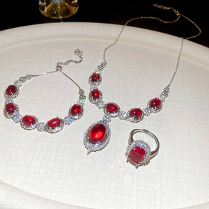 Detail of silver jewelry set with red gemstones and zircons on a textured plate